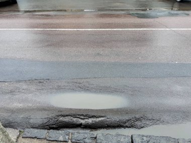 Yağmurdan sonra asfalt yolda büyük bir su birikintisi ve çukur oluşmuş. Kentsel altyapı sorunu, kötü yol bakımını ve hava durumunu temsil ediyor. Yüksek kalite fotoğraf