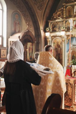 Uzhhorod, Ukrayna-6.10.2024. Bir kilisede Ortodoks vaftiz töreni. Altın cübbeli bir rahip ve havluya sarılı bebeği tutan vaftiz annesi..
