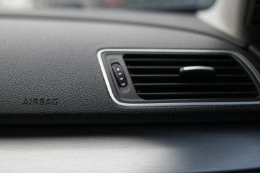 Gösterge panelindeki modern bir araba havalandırmasını kapat, parlak siyah ve gümüş tasarımlı, görünür hava yastığı etiketli, otomotiv içi detaylarını vurgulayan, yazılı hava yastığı. Yüksek kalite fotoğraf
