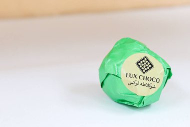 Uzhhorod, Ukrayna 11 Nisan 2025. Çikolatayı parlak yeşil folyoya sarıp, İngilizce ve Persçe olarak Lux Choco markalaştırdım. Hafif arkaplana yumuşak gölgeler yerleştirdim. Zarif şekerleme paketleme.
