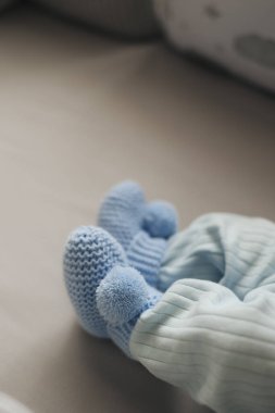Yumuşak mavi örgü patik ve çizgili pijama giyen yeni doğmuş bir bebeğin yakın çekimi. Çocukluk dönemi temaları, rahatlık ve erken dönem ebeveynliği için ideal, samimi ve iç açıcı bir görüntü..