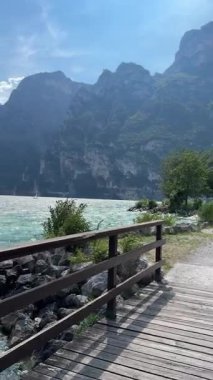 Arka planda görkemli dağlarla birlikte turkuaz alp gölü kıyısında tahta bir tahta kaldırım manzarası. Huzurlu bir yaz günü, seyahat ve rahatlama için mükemmel. Yüksek kalite 4k görüntü