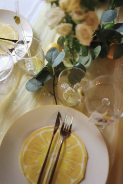 Beyaz tabaklar, altın çatal bıçak, bardaklar ve taze çiçeklerle süslü zarif bir limon temalı masa. Yaz düğünleri, bahçe partileri ya da şık ev dekorasyonu için mükemmel. Yüksek kalite fotoğraf