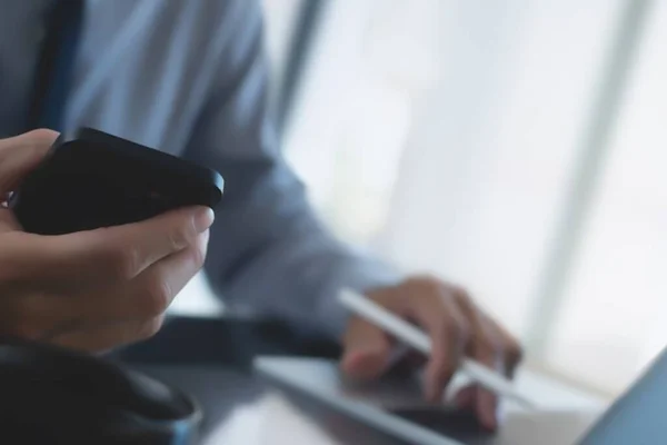 İşletme ve Finans. Ofiste dijital tablet ve dizüstü bilgisayar kullanan bir iş adamı. İşadamı çalışıyor, tablet ekranda dokunuyor ve dizüstü bilgisayarda yazıyor, iş verilerini araştırıyor, sörf yapıyor. 