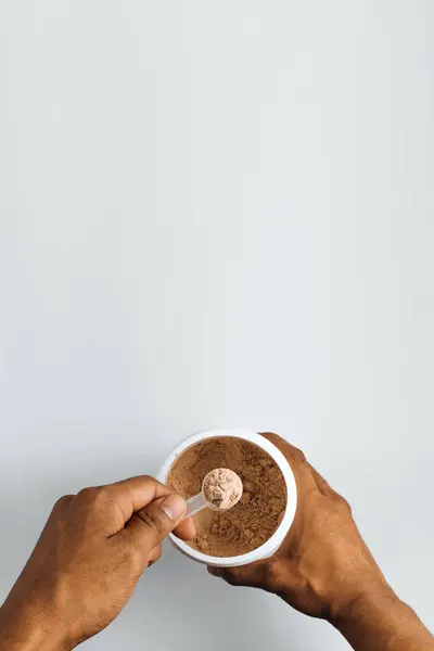 Beyaz arka planda bir kepçe toz vegan proteini tutan eller..