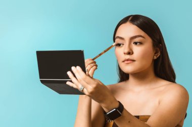 Makyaj yapan genç, mutlu ve güzel Latin Amerikalı kadın portresi.