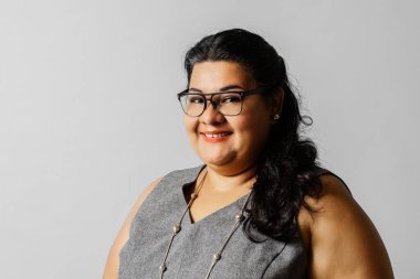 Büyük boy Latin Amerikalı yetişkin bir kadın. Gri arka planda gözlük ve takım elbise giyiyor. göz doktoru konsepti.