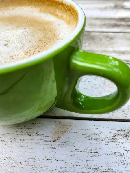 Milk coffee in a green mug on a white wooden table