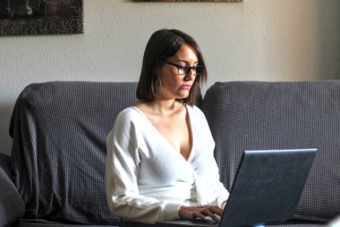 Genç beyaz kız bilgisayarını kanepeden kullanıyor. Evden çalışmak