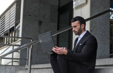 Sokakta bilgisayar kullanan takım elbiseli bir adam.