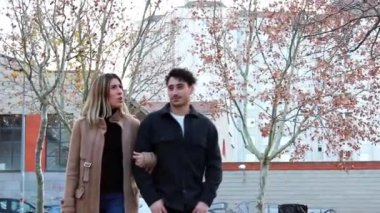 Mutlu genç beyaz çift parkta yürüyor, iyi giyimli, yarı vücut, el ele tutuşuyorlar..