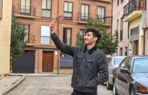 Cute guy just young white guy taking a selfie, curly hair, on the street, half body, seen from the outside