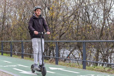 Şehrin varoşlarında, kasklı ve sırt çantalı, elektrikli scooter kullanan genç beyaz bir adam..