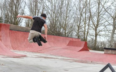 Siyah paten parkında paten kayan genç, siyah saçlı, kasksız, dinamik hareketlerle havada sıçrayan beyaz bir adam. Boşluğu kopyala