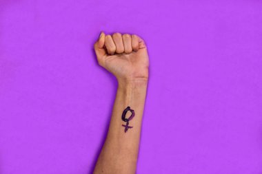 Menekşe arka planda bir kadının yumruğu kaldırılmış, kolunda bir kadının sembolü var. Feminist güç kavramı