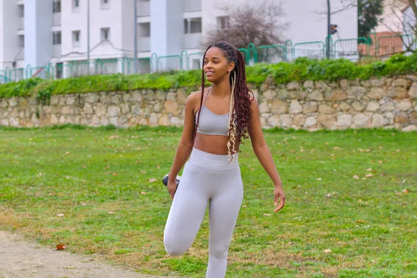 Young pretty black woman stretching her leg outdoor in sportswear, getting ready to run, looking away, front view, full length. Concept of running
