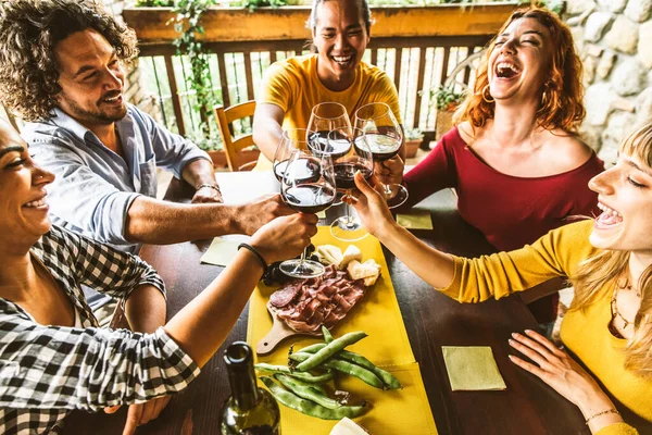 Multiracial people cheering red wine sitting outside at bar table