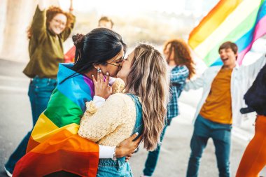 Lgbt topluluğunun konseptinde iki kız dışarıda öpüşüyor- sarı arka planda duran çok ırklı arkadaşlar