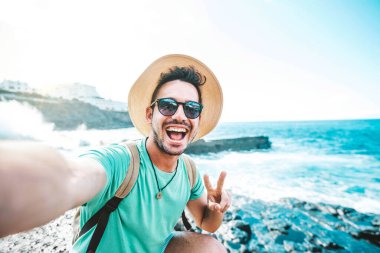 Yaz tatilinde selfie çeken yakışıklı genç adam - Macera yolculuğunda kameraya gülümseyen mutlu gezgin - teknoloji, seyahat ve insanlar konsepti