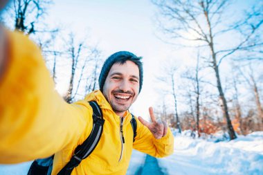 Sırt çantalı mutlu bir adam kışın buzlu ormanda selfie portresi çekiyor gülümseyen bir yürüyüşçü dağlara tırmanıyor spor, seyahat ve teknoloji konsepti