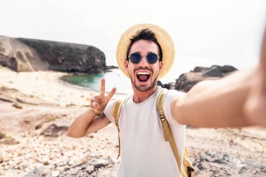 Yaz tatilinde şapkalı ve güneş gözlüklü yakışıklı adam selfie çekiyor. - Sırt çantalı mutlu yürüyüşçü dışarıda kameraya gülümsüyor.
