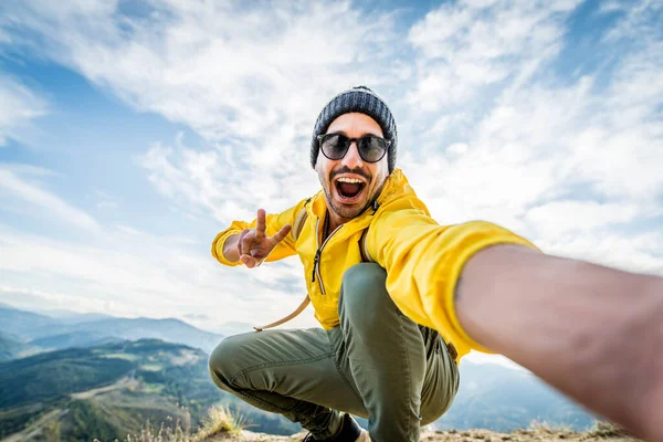 Genç yürüyüşçü dağın tepesinde selfie portresi çekiyor mutlu adam kameraya gülümsüyor yürüyüş yapıyor ve uçuruma tırmanıyor.