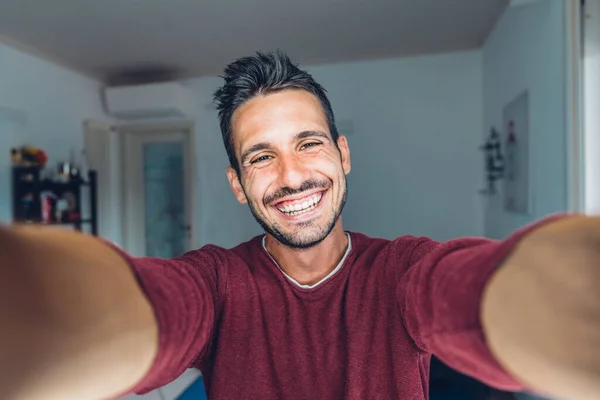 stock image Happy young handsome millennial man taking a selfie smiling at the camera in the living room at home