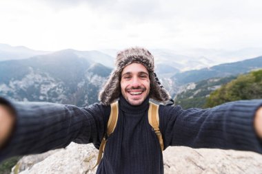 Yakışıklı genç yürüyüşçü bir dağın tepesinde selfie çekiyor. Adam kaya, spor, insanlar, yaşam tarzı ve teknoloji konseptine tırmanıyor..
