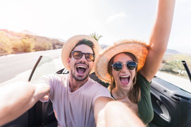 Mutlu ve güzel bir çift tatilde üstü açık bir arabayla selfie çektiriyorlar. Kiralık arabalar, tatiller ve insanlar.
