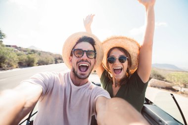 Mutlu ve güzel bir çift tatilde üstü açık bir arabayla selfie çektiriyorlar. Kiralık arabalar, tatiller ve insanlar.