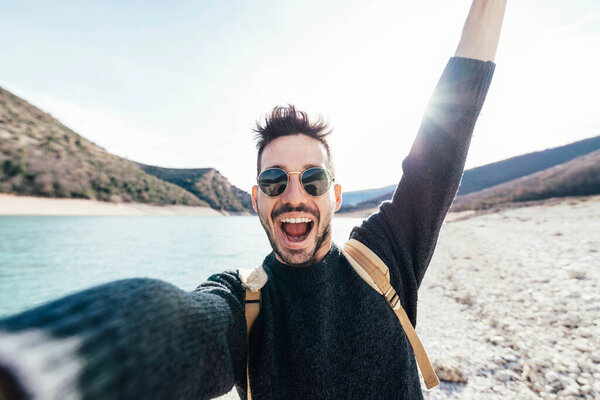 Красивый мужчина с рюкзаком делает селфи на природе - Мужской турист улыбается на камеру во время прогулки по горам - турист весело проводит время, исследуя живописный лес