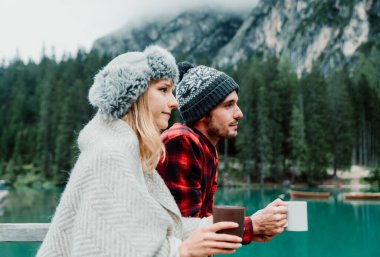 Braies Italya 'daki bir alp gölünü ziyaret eden iki yetişkinin romantik öpücüğü - Sonbahar dağlarında sıcak çikolata içen bir turist - çift, seyahat ve seyahat kavramı