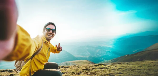 若いハイカーの男は 山の頂上にセルフィーの肖像画を取る カメラで微笑む幸せな男 スポーツライフスタイルとソーシャルメディアのインフルエンサーの概念 ストック画像