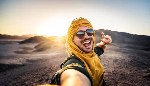 屋外でスマートな携帯電話でセルフィー写真を撮る旅行者 山の頂上に微笑む陽気な男 岩の砂漠で旅行するハイカー ストック写真