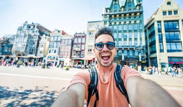 オランダのアムステルダムでセルフィー写真を撮るハッピーツーリスト 外でスマートフォンデバイスを使用して陽気な男 夏のヨーロッパの休暇を楽しむ学生旅行者 ライフスタイルの観光コンセプト ロイヤリティフリーのストック写真