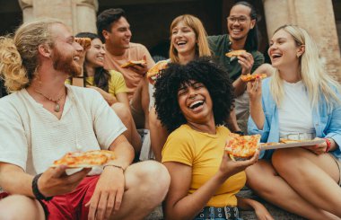 Çok kültürlü gülümseyen arkadaşlar dışarıda oturmuş pizza yiyorlar neşeli gençler yaz tatilinin tadını çıkarıyorlar güneşli bir günde kızlar ve erkeklerin takıldığı mutlu bir yaşam tarzı konsepti