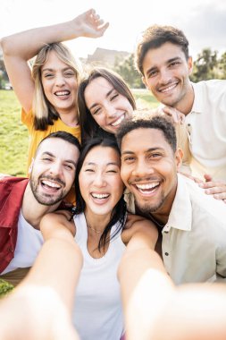Akıllı cep telefonu cihazıyla selfie çeken çok ırklı gençler - kameraya gülümseyen mutlu arkadaşların dikey fotoğrafı - yaz günü takılan erkek ve kızlarla yaşam tarzı konsepti 
