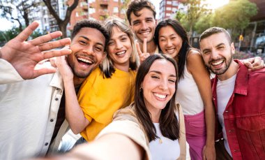 Çok kültürlü, neşeli arkadaşlar akıllı cep telefonu cihazıyla selfie çekiyorlar. Gençlik cemiyeti üyeleri kameraya birlikte gülüyorlar. Erkekler ve kızlarla dışarıda eğlenen arkadaşlık kavramı.