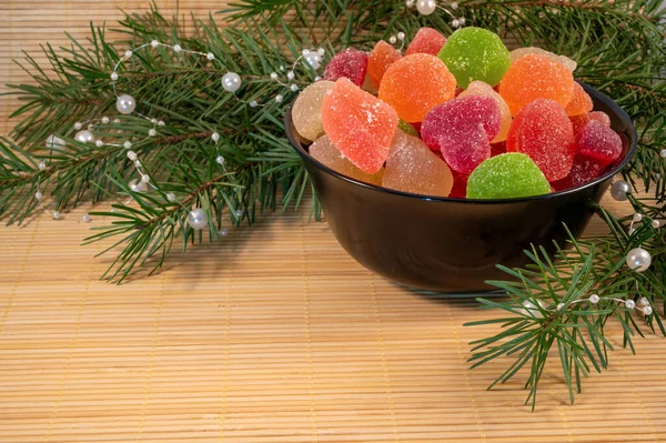 Siyah bir tabakta renkli jöle şekerleri ve ahşap bir arka planda noel ağacı dalları.