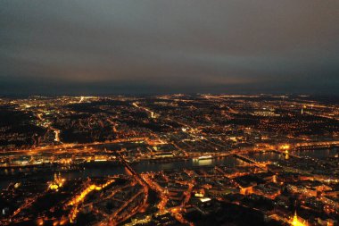 The image showcases a breathtaking aerial view of Prague at twilight, with the city's lights creating a warm, inviting glow that contrasts with the darkening sky. The city unfolds beneath as a tapestry of history and modernity, with the Vltava River 