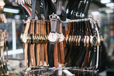 This image showcases a stunning variety of watches with leather straps displayed in a vibrant Brazilian marketplace. The focus on a singular watch with classic design elements, contrasted against the blur of diverse styles behind it, highlights the i