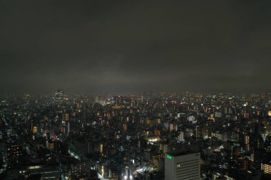 The sprawling urban expanse of Tokyo comes alive at night, with countless lights twinkling in the darkness. This aerial shot captures the immense scale and the dense layout of the city, offering a glimpse into the vibrant life of Japan's capital afte