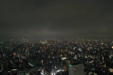 The sprawling urban expanse of Tokyo comes alive at night, with countless lights twinkling in the darkness. This aerial shot captures the immense scale and the dense layout of the city, offering a glimpse into the vibrant life of Japan's capital afte