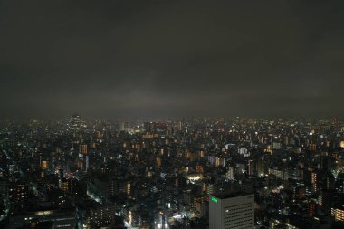The sprawling urban expanse of Tokyo comes alive at night, with countless lights twinkling in the darkness. This aerial shot captures the immense scale and the dense layout of the city, offering a glimpse into the vibrant life of Japan's capital afte