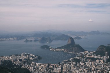 The sprawling cityscape of Rio de Janeiro is a stunning mosaic of urban life, bordered by the iconic shapes of mountainous terrain and the expansive Atlantic Ocean. The tranquil waters reflect the vastness of the city, offering a serene counterpoint 