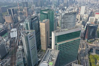 A dynamic perspective of Tokyo's bustling city life, highlighting the intricate train tracks amidst towering skyscrapers under a clear sky.