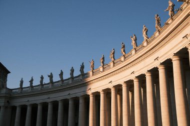 A dramatic perspective of the iconic colonnades in St. Peter's Square, Rome, as the day's last light casts shadows on the statues.