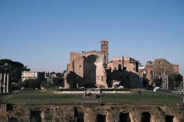 The Roman Forum, a plaza rich with history, is bathed in sunlight, revealing the intricate details of its ruins. Once the epicenter of Roman public life, it now stands as a testament to the empire's legacy in the heart of Rome.