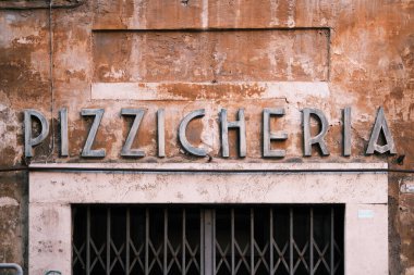 The vintage signage of 'Pizzicheria' etched onto the weathered facade of a Roman building speaks volumes of the city's culinary traditions and the timeless charm that pervades the streets of Rome, inviting locals and tourists alike.