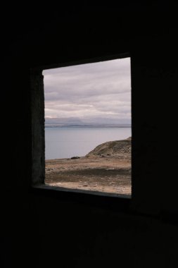 Peering through an ancient window frame in Jordan, one is treated to a mesmerizing view of the Dead Sea, its tranquil waters bordered by the rugged landscape. This framed perspective offers a unique vantage point, blending historical architecture wit
